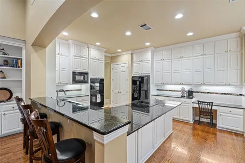 a kitchen with stainless steel appliances granite countertop a stove a sink a refrigerator and white cabinets with wooden floor