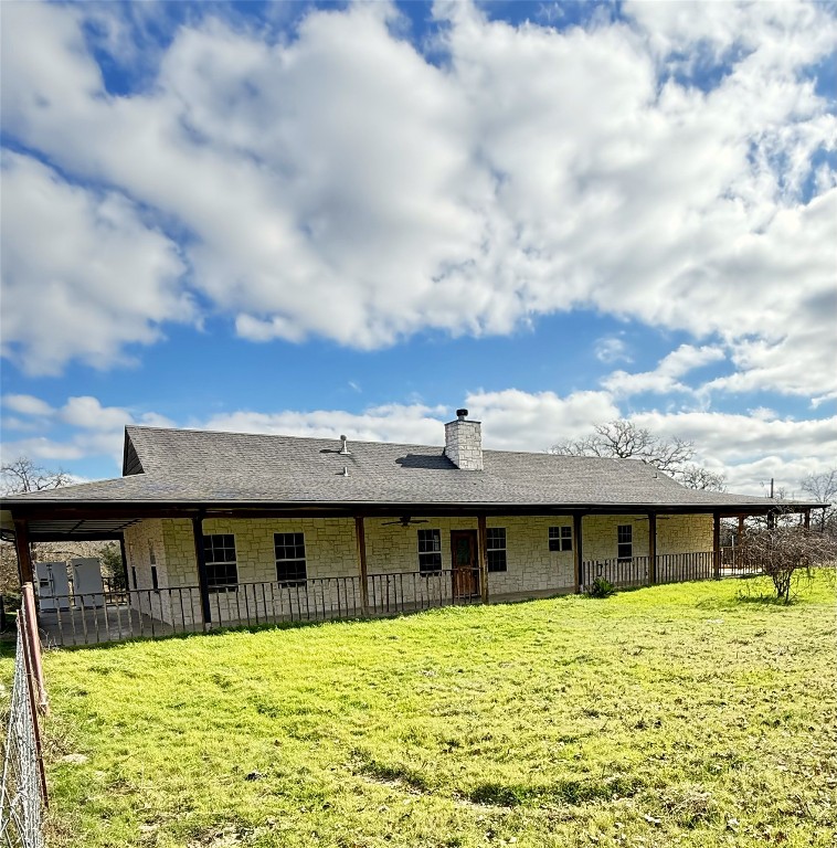 Rear view of house with roof with shingles, a chimney, stone siding, and a yard