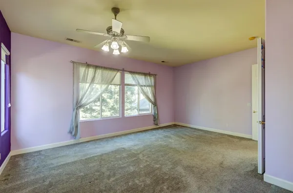 an empty room with a chandelier fan and windows