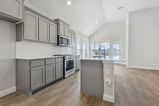 a kitchen with stainless steel appliances granite countertop a stove top oven a sink and white cabinets with wooden floor