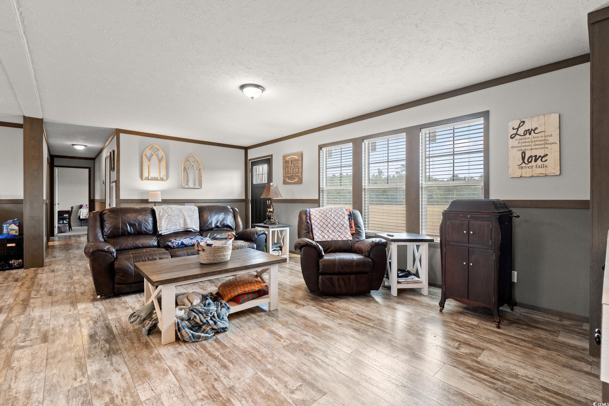 Living room featuring a textured ceiling, ornamental molding, and light wood-type flooring