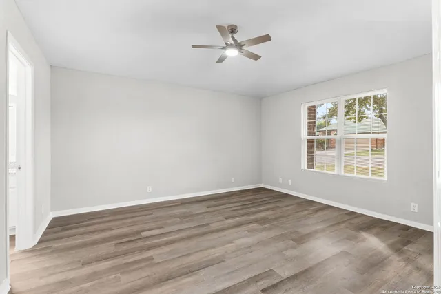 an empty room with wooden floor ceiling fan and windows