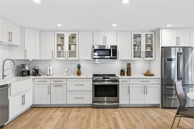 a kitchen with stainless steel appliances granite countertop a stove top oven a refrigerator a sink and white cabinets with wooden floor