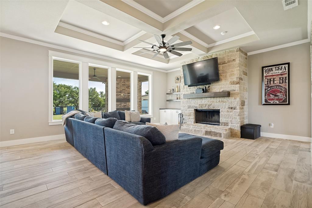 6913 Veal Station Road Weatherford, TX 76085 - Photo 4 of 31 Living area featuring a stone fireplace with a wood mantle, wood-finish flooring, and a multi-tiered tray ceiling