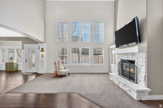 14714 South Bright Wood Road Herriman, UT 84096 - Photo 9 of 41 Carpeted living room with a towering ceiling, arched walkways, wood-type flooring, a stone fireplace, and healthy amount of natural light