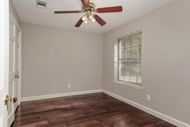 an empty room with wooden floor chandelier fan and windows