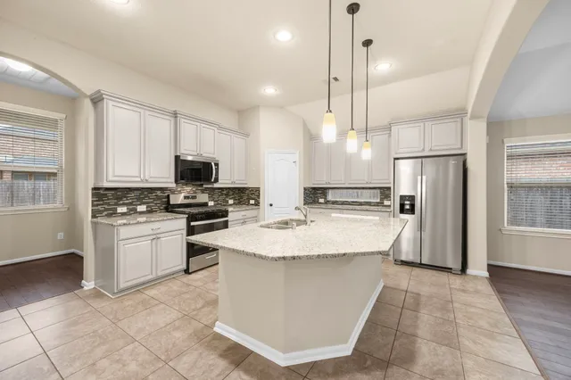 a large kitchen with granite countertop a stove a sink dishwasher a refrigerator and white cabinets with wooden floor