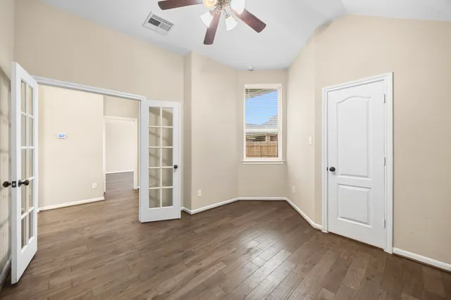 an empty room with wooden floor a ceiling fan and windows