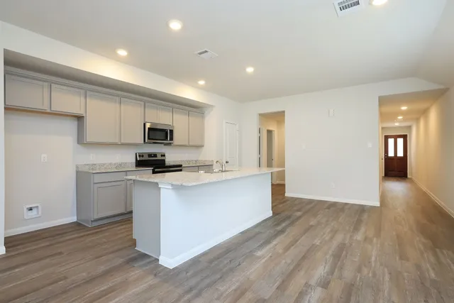 a kitchen with stainless steel appliances granite countertop a stove top oven a sink dishwasher and a refrigerator with wooden floor