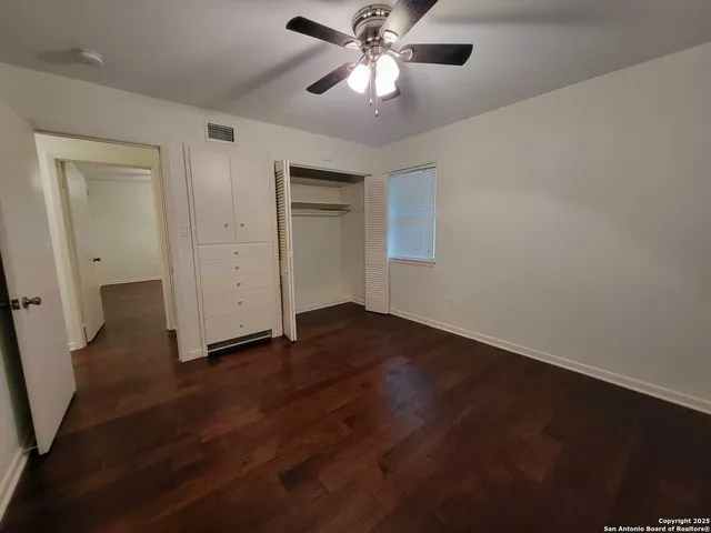 an empty room with wooden floor fan and windows