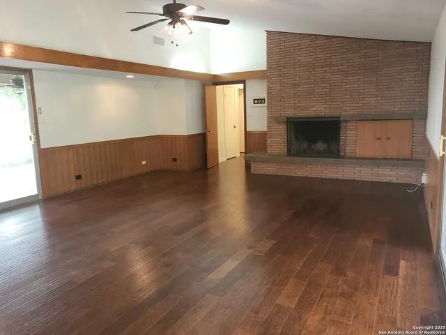 an empty room with wooden floor fireplace and windows