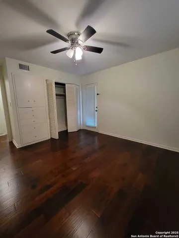 a view of an empty room with wooden floor and a ceiling fan