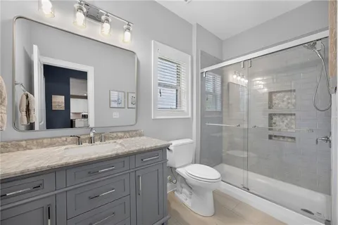 a bathroom with a granite countertop toilet a sink a mirror a shower a vanity and window