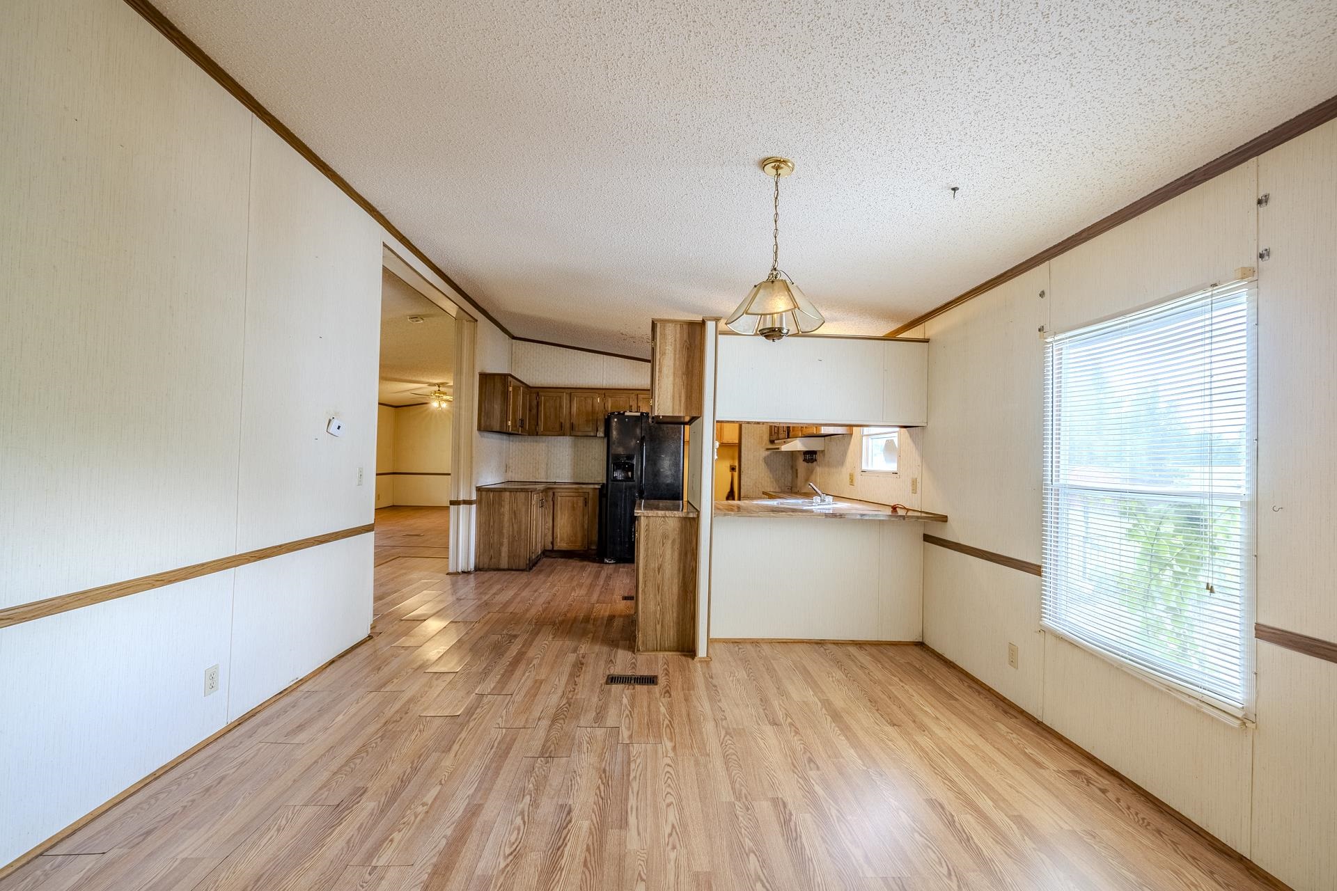 859 Old Morris Chapel Road Adamsville, TN 38310 - Photo 25 of 39 Open-concept interior featuring wood-finish flooring, a kitchen with dark cabinetry and a black refrigerator, and a window with blinds