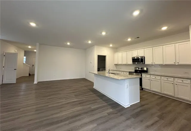 a view of kitchen with kitchen island granite countertop a stove top oven a sink and a refrigerator with wooden floor