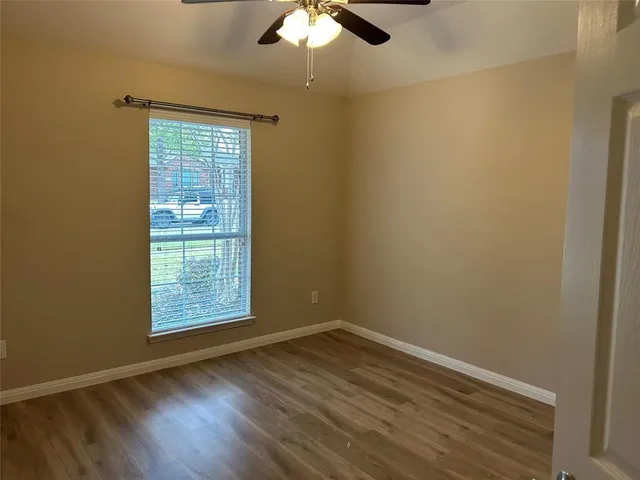 an empty room with wooden floor chandelier fan and windows