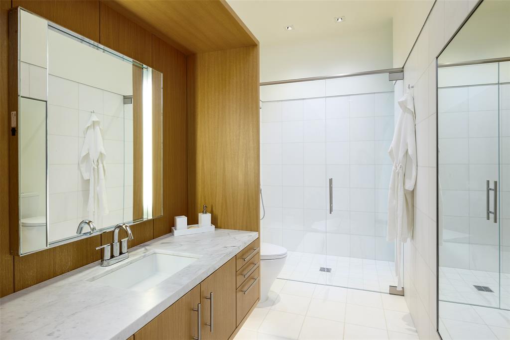 3511 Springbrook Street Dallas, TX 75205 - Photo 25 of 38 Modern bathroom featuring an integrated sink with a chrome faucet, a stone countertop, light wood-finish cabinetry, a glass-enclosed shower, and white tile flooring