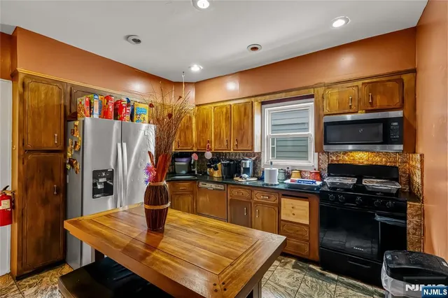 a kitchen with stainless steel appliances granite countertop a refrigerator a stove top oven a sink and dining table