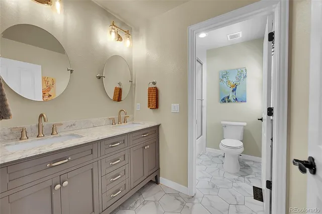 a spacious bathroom with a toilet a double vanity sink and a mirror