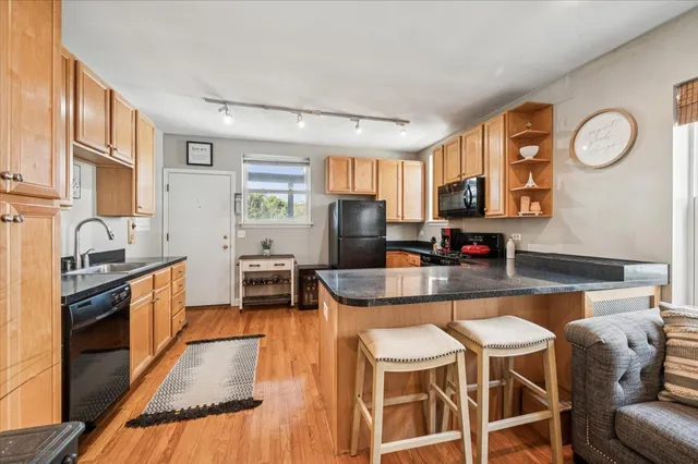 a kitchen with stainless steel appliances granite countertop a stove top oven a sink a dining table and chairs with wooden floor