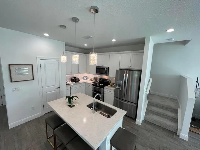a kitchen with stainless steel appliances a refrigerator a sink dishwasher a stove and white cabinets with wooden floor