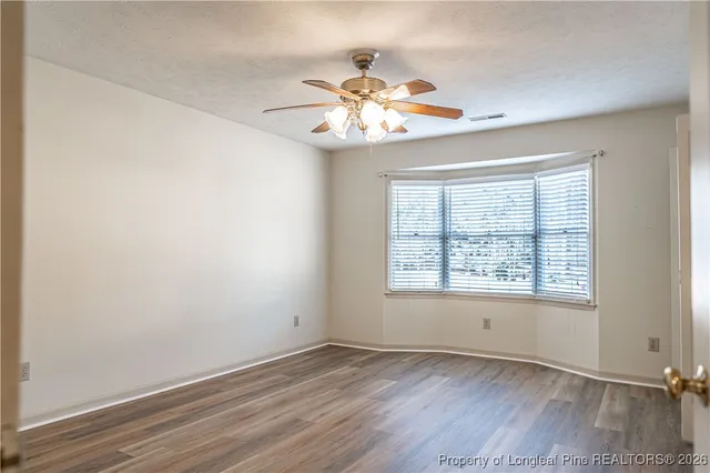 an empty room with wooden floor chandelier fan and windows