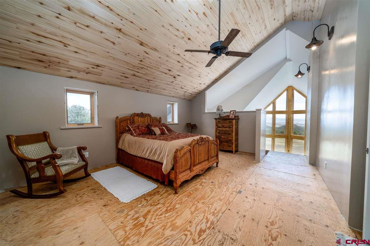 20885 Mesawood Road Cedaredge, CO 81413 - Photo 26 of 35 a spacious bedroom with a bed a chandelier and a window