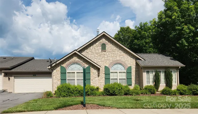 a view of a white house with large windows and a yard with plants and large trees