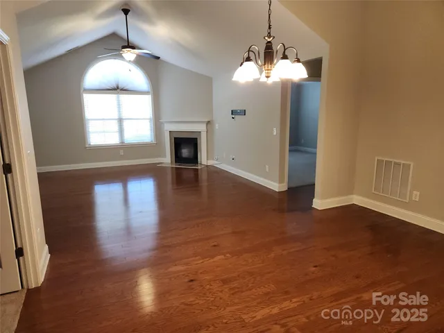 an empty room with wooden floor chandelier and windows
