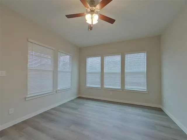 an empty room with wooden floor ceiling fan and windows