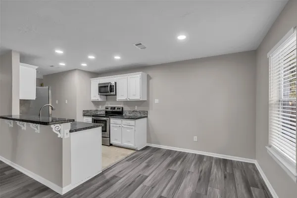 a kitchen with stainless steel appliances granite countertop a stove top oven a sink dishwasher and a refrigerator with wooden floor