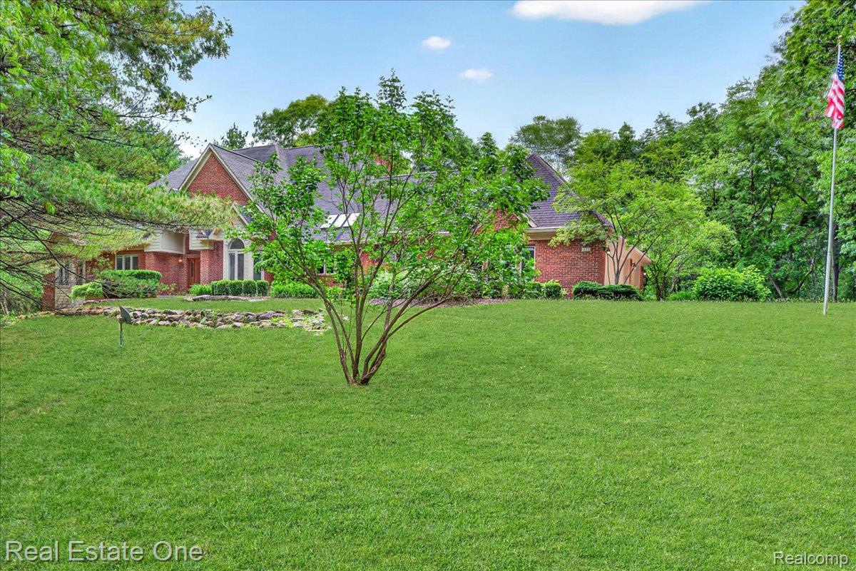 425 Courtney Road Leonard, MI 48367 - Photo 66 of 89 Expansive lawn with mature trees, brick exterior, arched entryway, and dark-pitched roof