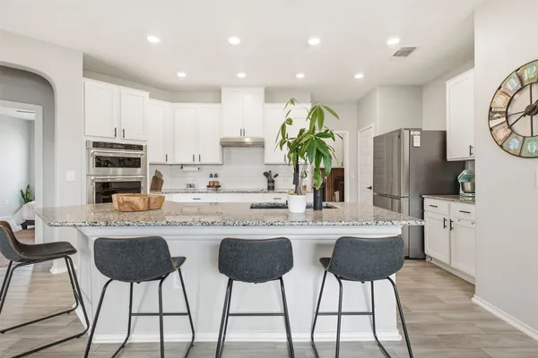 a kitchen with stainless steel appliances kitchen island granite countertop a dining table chairs refrigerator and microwave