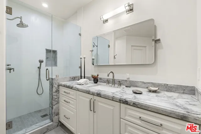 a bathroom with a granite countertop sink a mirror and shower
