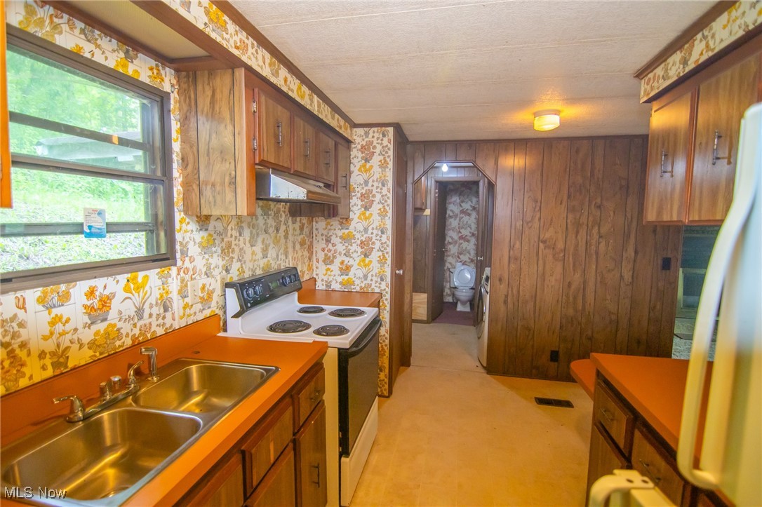 Kitchen featuring range with electric cooktop, a sink, under cabinet range hood, freestanding refrigerator, and brown cabinetry