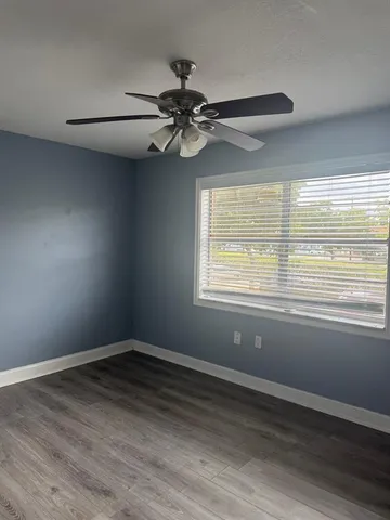 an empty room with a chandelier fan and wooden floor