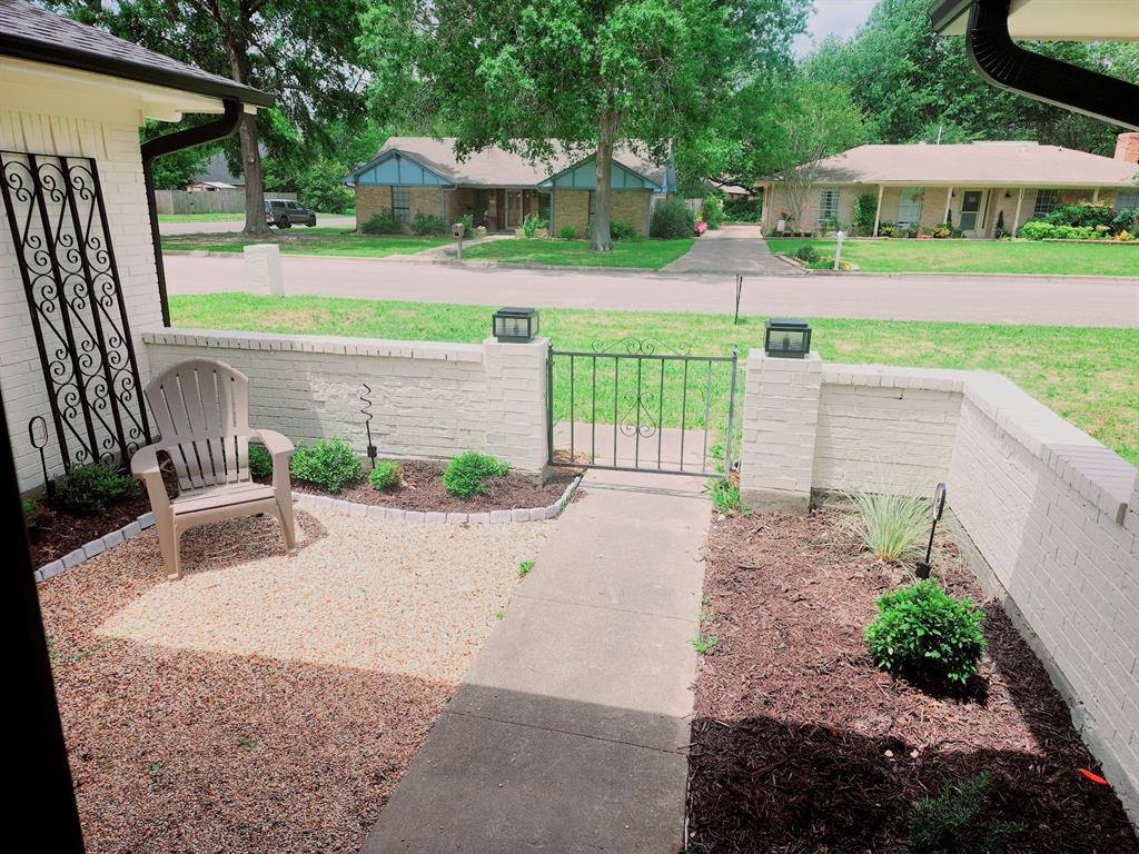 2908 Washington Street Commerce, TX 75428 - Photo 29 of 29 Front courtyard featuring a concrete pathway, decorative wrought iron gate, painted brick half-walls, and landscaped beds with various plantings