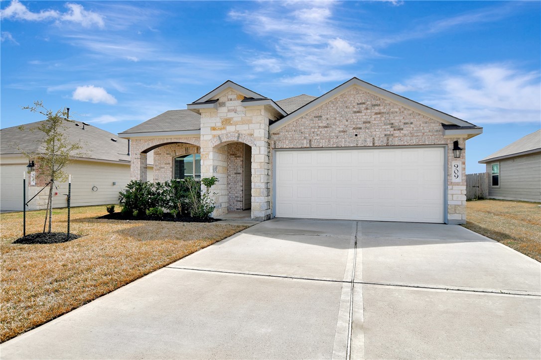 909 Davy Street Brenham, TX 77833 - Photo 3 of 35 Home featuring an attached garage, concrete driveway, a front lawn, and stone siding