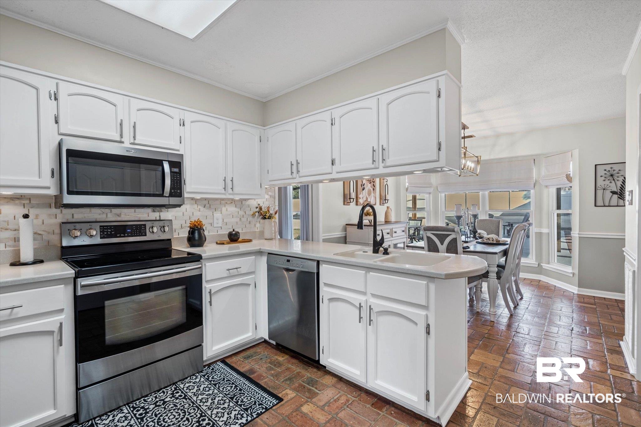 4567 Pine Avenue Saraland, AL 36571 - Photo 9 of 48 Kitchen with a peninsula, stainless steel appliances, white cabinets, and brick floors