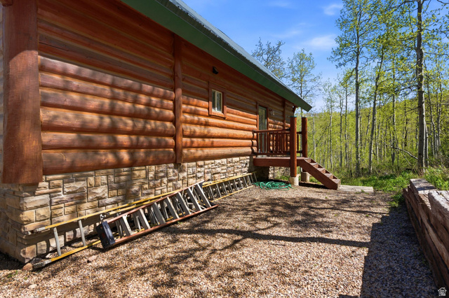 2096 South Aspen Ridge Coalville, UT 84017 - Photo 37 of 44 Wood-sided log cabin with a stone foundation, featuring a wood deck and stairs, set against a backdrop of mature trees