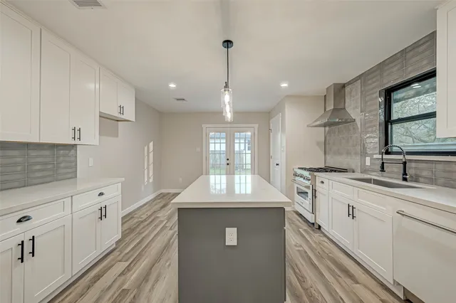 a large kitchen with granite countertop a sink dishwasher a stove and white cabinets with wooden floor