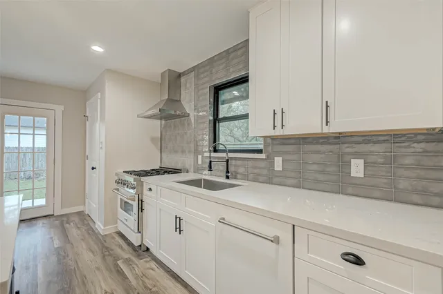 a kitchen with a sink dishwasher a stove and white cabinets with wooden floor