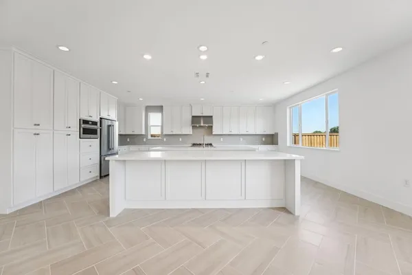 a large white kitchen with kitchen island a sink a center island stainless steel appliances and a cabinets