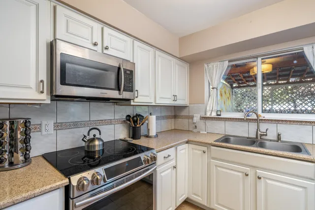 a kitchen with stainless steel appliances granite countertop white cabinets a stove a microwave and a sink
