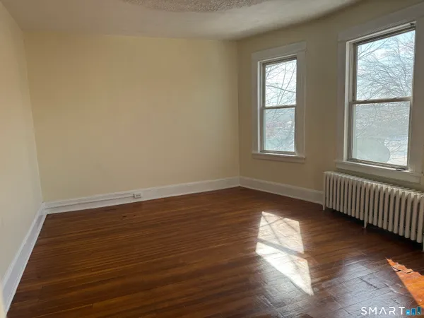 a view of an empty room with wooden floor and a window