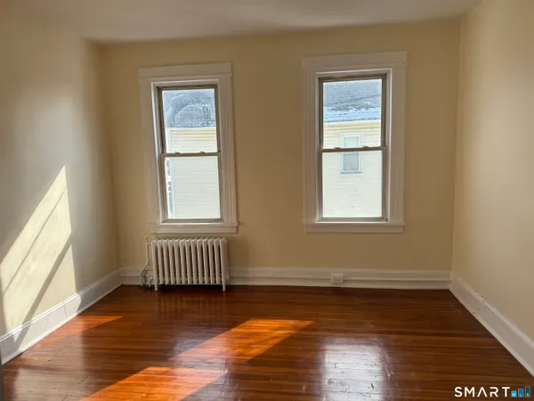 a view of an empty room with wooden floor and a window