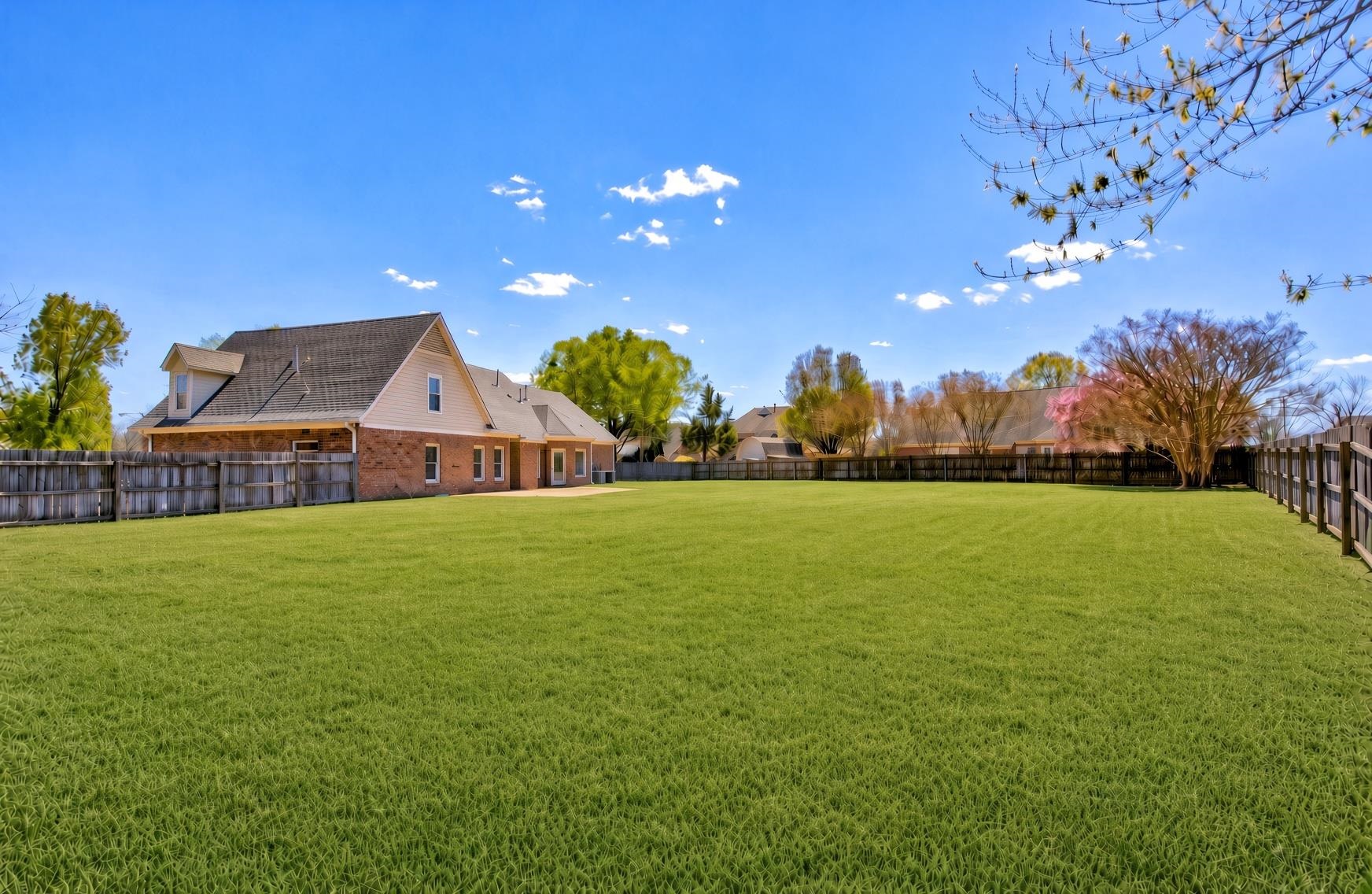 737 Steeple Ridge Cove Collierville, TN 38017 - Photo 2 of 21 Expansive grassy backyard featuring a full perimeter fence, mature trees, and a brick exterior home with a dormer window
