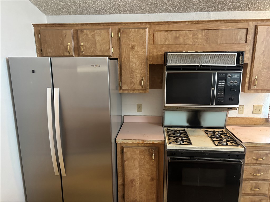 3871 Mormon Flat Road Golden Valley, AZ 86413 - Photo 23 of 52 The kitchen features wood cabinetry with gold-toned hardware, a stainless steel side-by-side refrigerator, and a black range with an integrated microwave and overhead exhaust fan