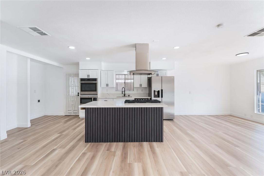 4980 Ridge Drive Las Vegas, NV 89103 - Photo 10 of 36 Kitchen featuring stainless steel appliances, island exhaust hood, light wood-style flooring, a kitchen island, and white cabinetry