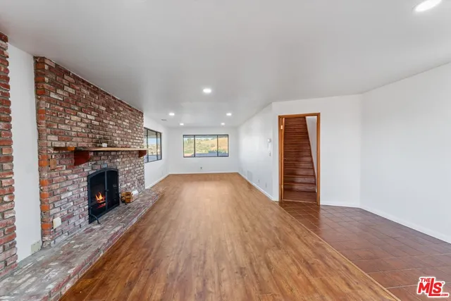 a view of an empty room with wooden floor fireplace and a window